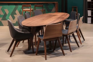 Ovale houten vergadertafel met zes houten stoelen met grijze bekleding in moderne kantoorruimte met groene muur.
