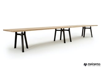 Lange houten vergadertafel met natuurlijke afwerking op drie zwarte trapeziumvormige onderstellen, tegen witte achtergrond.