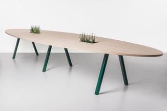 Ovale vergadertafel met hout kleuring blad, groen metalen poten, twee plantenbakken in het tafelblad.