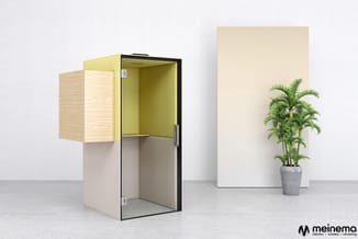 Gele en beige akoestische belcel met open deur, houten bovenpaneel en zwart frame, naast potplant en witte paneel in showroom