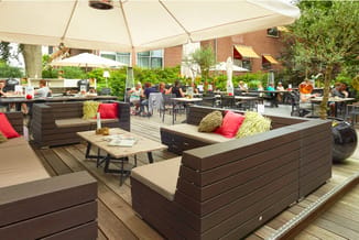Terrasoverkapping met zwarte loungebanken, rode kussens, houten tafels en parasols. Zitgroepen met bezoekers in ontspannen sf