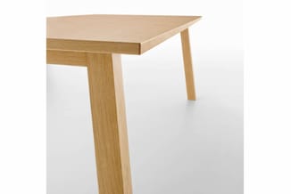 Houten vergadertafel met licht natuurkleurig blad en houten poten in houtnerf, gedeeltelijk zichtbaar tegen witte achtergrond