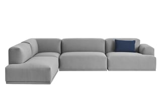 Grijze modulaire hoekbank met vier zitdelen, afgerond design en donkerblauw kussen op rechter zitgedeelte.