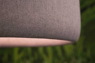 Grijze stofbekleding met textuurdetail op zitmeubel, roze/nudes poot zichtbaar, groene achtergrond.