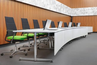 Moderne vergadertafel met witte bovenkant en aluminium onderstel, omringd door zwarte ergonomische bureaustolen met groene zi