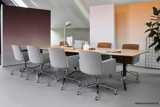 Vergaderruimte met rechthoekige tafel, grijze stoelen op wieltjes, bruine accenten, witte hanglamp, kleurrijke panelen aan wa