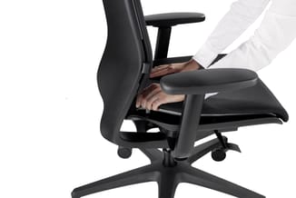 Zwarte ergonomische bureaustoel met netbespanning, armleuningen en zwarte wielen. Persoon in wit hemd zit erop en stelt de zi