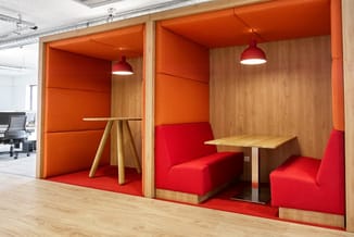 Twee houten akoestische boxen met oranje binnenwanden, rode zithoeken, houten tafels en rode hangende lampen in kantoorruimte