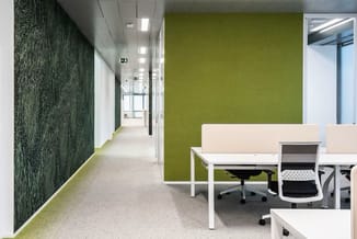 Modern kantoor met groene wand, witte bureau's, zwarte kantoorstoelen en textiele wandbekleding in donkergroen.