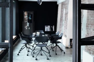Moderne vergaderruimte met zwart rond tafelblad, vier zwarte ergonomische stoelen op wieltjes, zwarte wand met inspiratiebord