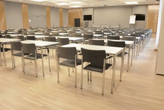 Grote zaalbijzettafels met grijze stoelen, rijen rechthoekige witte tafels met metalen poten in moderne vergaderruimte.
