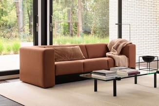Terracotta bank met modulair design in moderne kantoorruimte met glazen wand, zwarte tafel met boeken en beige vloerkleed.