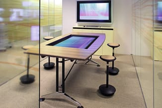 Moderne vergaderkamer met interactieve tafel met geïntegreerd aanraakscherm, houten blad, zwarte poten op wielen, bijzettafel