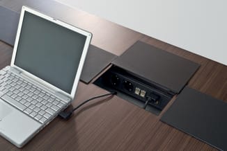 Witte netbook op houten bureau naast zwarte bureauvoeding met stopcontacten en USB-poorten, zwarte muismat ernaast.