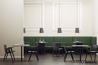 Moderne restaurantruimte met groene zitbank, zwarte stoelen, zwarte tafels, hangende lampen en grote ramen met zonwering.