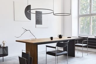 Moderne vergaderruimte met houten tafel, zwarte stoelen, hangende circulaire verlichting en wandkunst tegen witte muur.