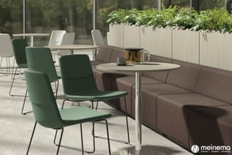 Moderne kantoorlounge met groene stoelen met zwart frame, ronde tafel met witte blad, bruine bank en plantenbakken achter gro