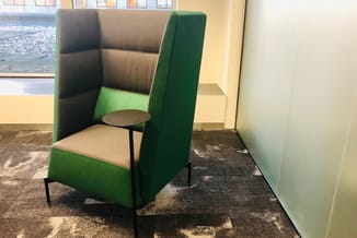 Groene en grijze akoestische belcel met bijzettafel in kantoorruimte met geel-beige wanden.