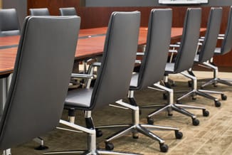 Vergadertafel met grijze bureaukstoelen op wielen, houten tafelblad, moderne kantoorinrichting.