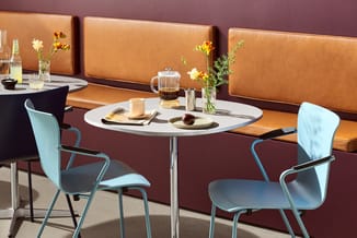 Moderne kantoorruimte met rond wit tafeltje, lichtblauwe stoelen, caramelkleurige leren zitbank en paarse wand. Tafel gedekt