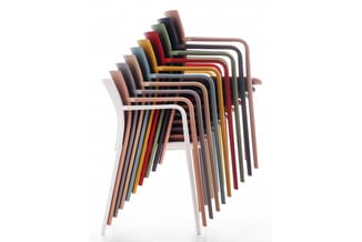 Stapel gestapelde kunststof stoelen in verschillende kleuren, waaronder wit, beige, rood, geel, groen, grijs en zwart, met ge