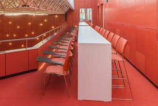 Vergaderruimte met rode wanden, rode stoelen met zwarte zittingen aan witte tafel, rode vloer, spotverlichting en ronde dakst