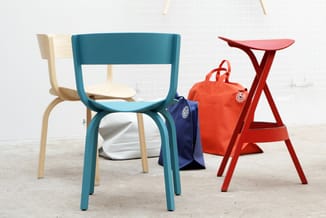 Toonkamer met drie kleurrijke stoelen: turquoise stoel met houten poten, crèmekleurige stoel op achtergrond, rode tripod-tafe