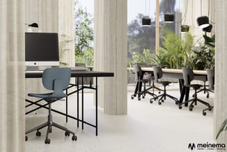 Modern kantoor met grijsblauwe bureaustoel aan zwarte tafel met iMac, hanglampen, betonnen zuilen, grote ramen en groene plan