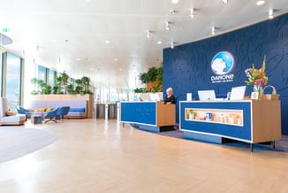Danone kantoor receptie met blauwe wandpanelen, houten receptiondesks, blauwe design stoelen, witte plafondverlichting en gro