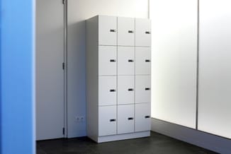 Witte kastenwand met 12 vakken in 3x4 configuratie, elk voorzien van een zwart slot, opgesteld in een moderne kantoorruimte m
