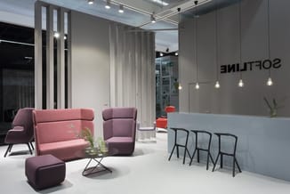 Modern kantoorlounge met roze stoffen zitmeubels, zwarte barkrukken bij witte balie met 'Soutine' opschrift, hangende verlich