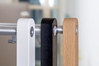 Drie garderobe hangers in wit, zwart en naturel hout, gemonteerd op een metalen rail.