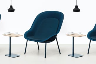 Blauwe loungefauteuil met zwarte metalen poten naast houten bijzettafels met koffie en notitieboeken, hangende zwarte lampen