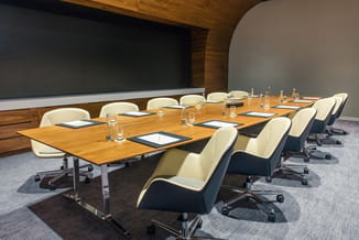 Moderne vergaderzaal met houten tafel, creme en zwarte kantoorstoel met wieltjes, waterkaraffen, notitieblokken, grote zwart