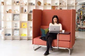 Rode akoestische werkplek met hoge zijwanden, vrouw aan laptop, metalen onderstel, geïntegreerd tafeltje, in open kantoor met