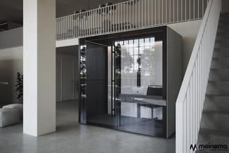 Moderne belcel met zwart frame en glazen wanden in kantoorruimte met betonnen vloer, witte zuilen en metalen trap.