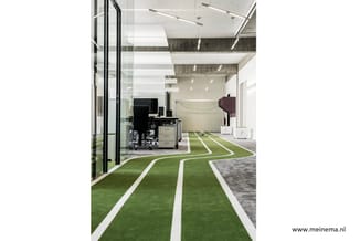 Modern kantoor met groen kunstgrasvloer en witte lijnen, zwarte bureaustoel, grijze archiefkast, beige akoestische paneel en