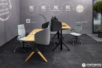 Kantoorinrichting met houten bureaus, grijze draaistoelen, zwarte tafelpoten en circulaire economie-schema op grijze wand.