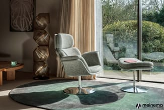 Modern loungezitje met grijze fauteuil en ottoman op wielbasis, rond groen-grijs tapijt, houten bijzettafel en decoratieve ho