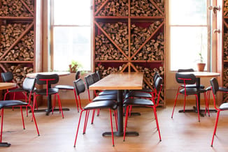 Moderne kantoorruimte met houten tafel, rode stoelen met zwarte zitting, grote ramen en gestapelde brandhoutmuur op achtergro