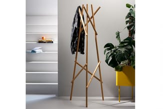 Houten garderobe met X-vormig design, beladen met donker kledingstuk, in kantoorruimte naast gele plant pot en grijze wandkas