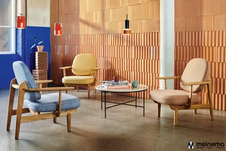 Moderne lounge met drie houten fauteuils in blauw en beige textiel, ronde zwarte salontafel, terracotta baksteenpatroon op wa