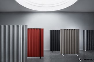 Akoestische scheidingswanden in verschillende kleuren (grijs, rood, zwart, beige) in moderne showroom met ronde plafondlamp.