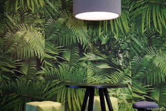Zwarte staande lamp met grijze kap boven zwarte tafel in ruimte met groen bladmotief wandbekleding.