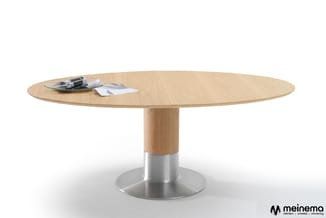 Ronde vergadertafel met naturel houten blad en voet, metalen zilveren voetring, met pennen en papier op het tafelblad.