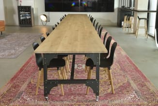 Lange vergadertafel met natuurlijke houttafelblad en zwart stalen frame, omgeven door stoelen met roze en zwarte bekleding op
