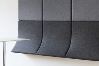Grijze akoestische wandpanelen in modulaire opstelling met gebogen vormen, getoond met klein bijzettafeltje in kantooromgevin