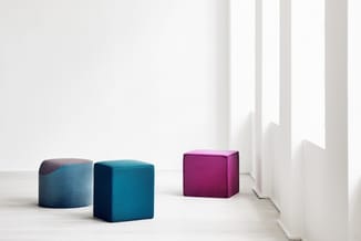 Drie gestoffeerde poeven in een minimalistisch interieur: twee blauwe poeven links (één cilindervormig, één kubusvormig) en é