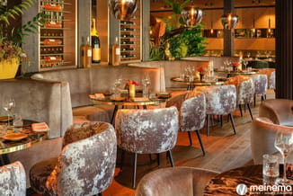Luxe restaurantinterieur met grijze fluwelen banken, fluweelkruk-stoelen in grijs-bruin, ronde glazen tafels, houten vloer en
