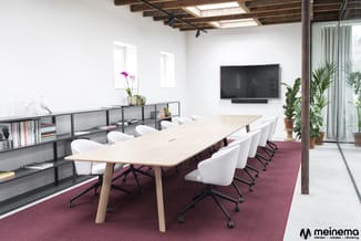 Moderne vergaderruimte met lichte houten vergadertafel, witte bureautoelen op wielen, grijze open kasten, tv-scherm aan wand,